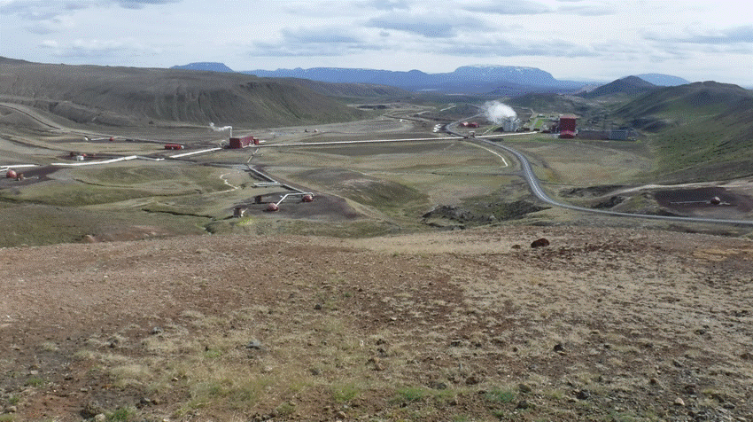 Photo looking down into a shallow volcanic valley in the mountains of Iceland, showing geothermal wells and associated piping connecting to a geothermal power station
