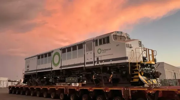 Large white battery-electric rail locomotive, mounted on a large road trailer with dozens of wheels